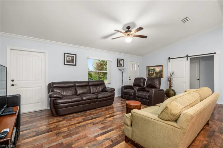 Living area with crown molding, a barn door, dark wood-style flooring, a ceiling fan, and vaulted ceiling