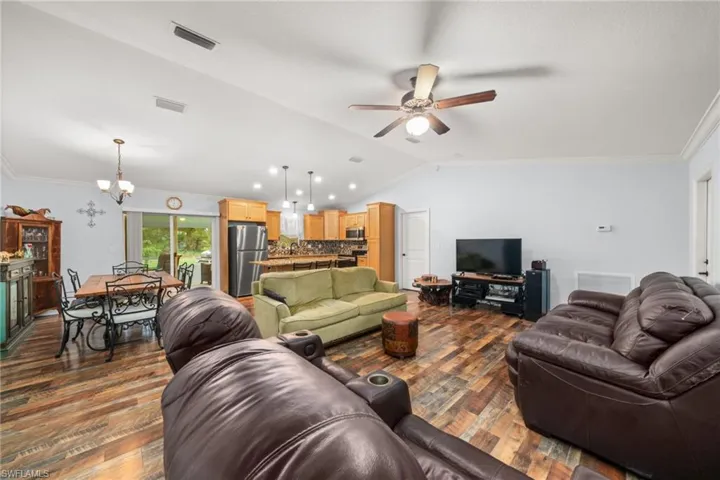 Living room with lofted ceiling, a chandelier, ornamental molding, dark wood finished floors, and a ceiling fan