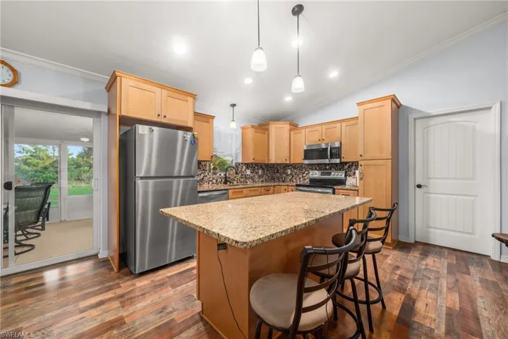 Kitchen with ornamental molding, stainless steel appliances, decorative light fixtures, light stone countertops, and tasteful backsplash