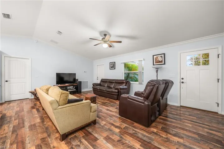 Living room with crown molding, dark wood finished floors, vaulted ceiling, and a ceiling fan