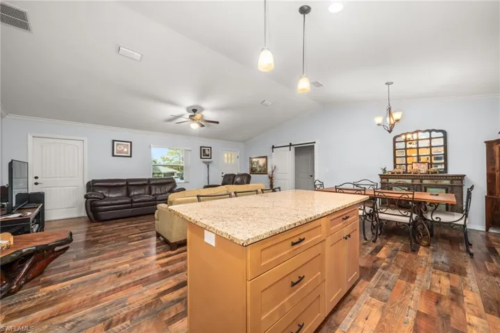 Kitchen featuring a barn door, ornamental molding, light stone counters, pendant lighting, and dark wood-type flooring