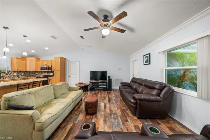 Living room with vaulted ceiling, dark wood-style flooring, a ceiling fan, and crown molding