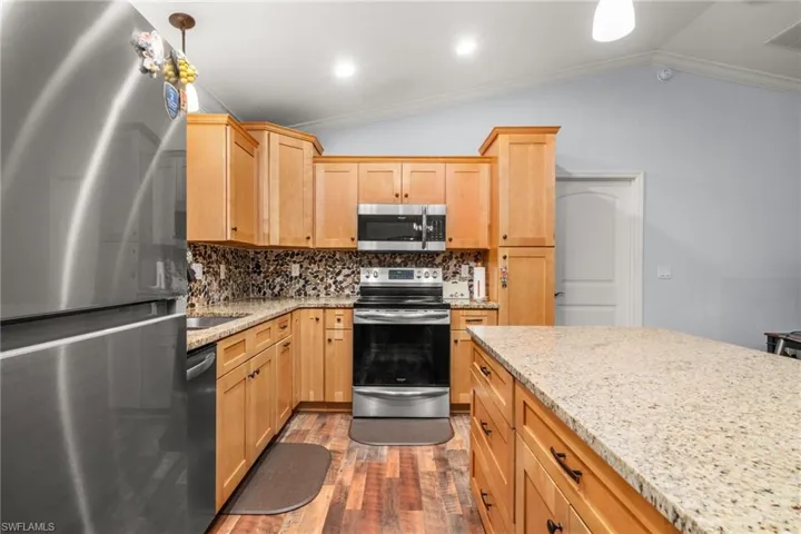 Kitchen with appliances with stainless steel finishes, tasteful backsplash, light stone countertops, vaulted ceiling, and light brown cabinetry