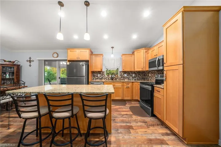 Kitchen featuring decorative backsplash, appliances with stainless steel finishes, dark wood-style flooring, a breakfast bar, and a center island