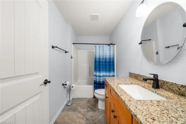 Full bathroom featuring shower / bath combination with curtain, vanity, and light stone finish floors