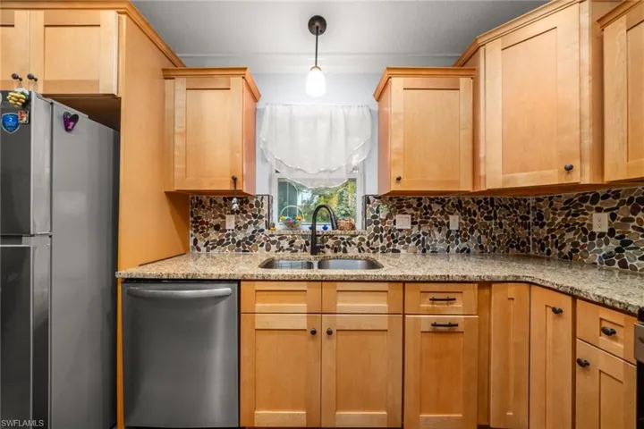 Kitchen with appliances with stainless steel finishes, light stone counters, pendant lighting, and light brown cabinetry