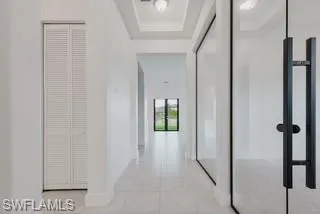 Hall featuring a tray ceiling and light tile patterned floors