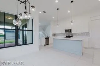 Kitchen with white cabinetry, hanging light fixtures, light countertops, a center island, and light tile patterned floors
