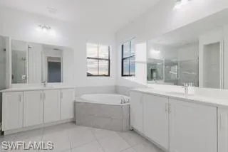 Full bath featuring a stall shower, a bath, two vanities, and light tile patterned floors