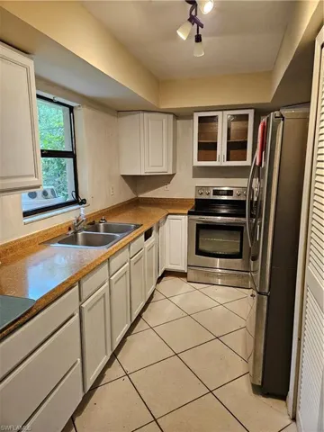 Kitchen with fridge, range, light tile patterned floors, sink, and white cabinets