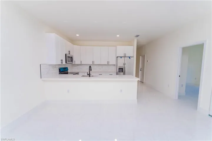 Kitchen featuring decorative backsplash, appliances with stainless steel finishes, a peninsula, and light countertops