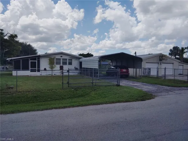 Fenced property with a screened porch, carport, and a detached garage structure featuring two roll-up doors