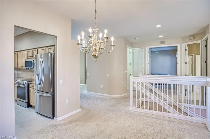 Kitchen with hanging light fixtures, stainless steel appliances, backsplash, a chandelier, and light carpet