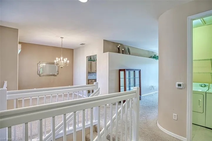 Corridor featuring a chandelier, light carpet, and washer and dryer