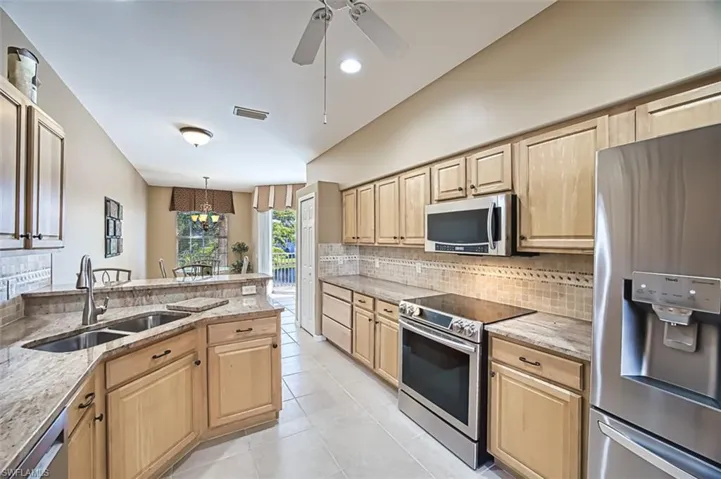 Kitchen featuring light stone countertops, appliances with stainless steel finishes, decorative light fixtures, and sink