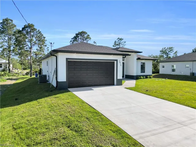 View of front of property with stucco siding, central AC unit, driveway, and a garage