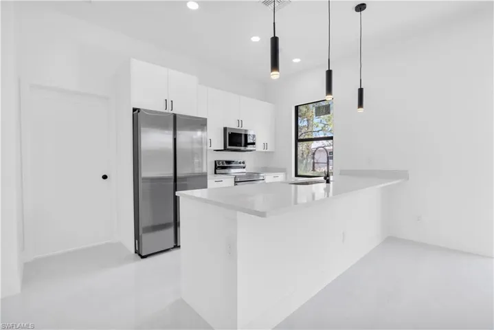 Kitchen with appliances with stainless steel finishes, a sink, a peninsula, recessed lighting, and white cabinets