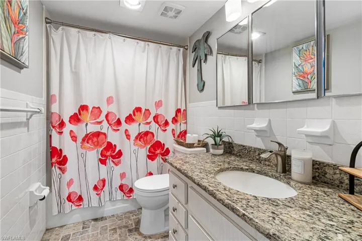 Full bathroom featuring vanity, shower/tub combo with curtain, toilet, and tile walls