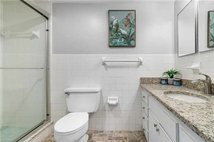 Bathroom with toilet, vanity, tile walls, and a shower with door