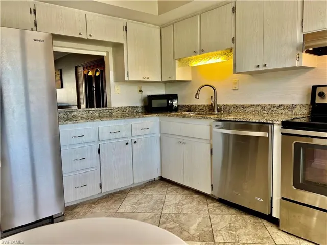 Kitchen with sink, cream cabinetry, ceiling fan, stainless steel appliances, and dark stone counters