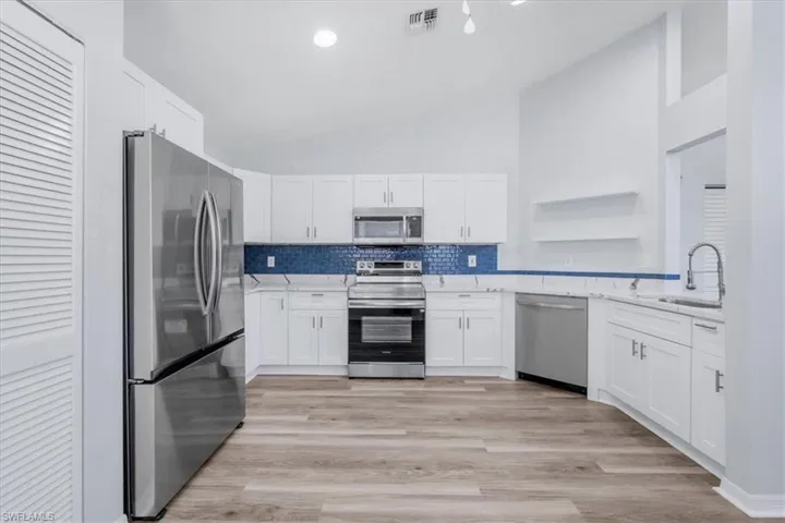 Kitchen with appliances with stainless steel finishes, white cabinets, backsplash, light wood-style floors, and light stone counters