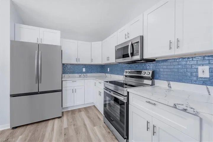 Kitchen with appliances with stainless steel finishes, white cabinetry, light stone countertops, and tasteful backsplash