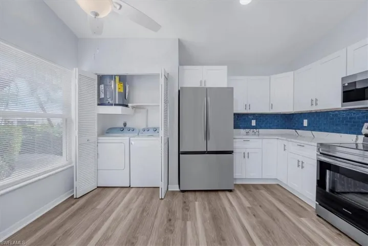 Kitchen featuring appliances with stainless steel finishes, white cabinets, water heater, separate washer and dryer, and decorative backsplash