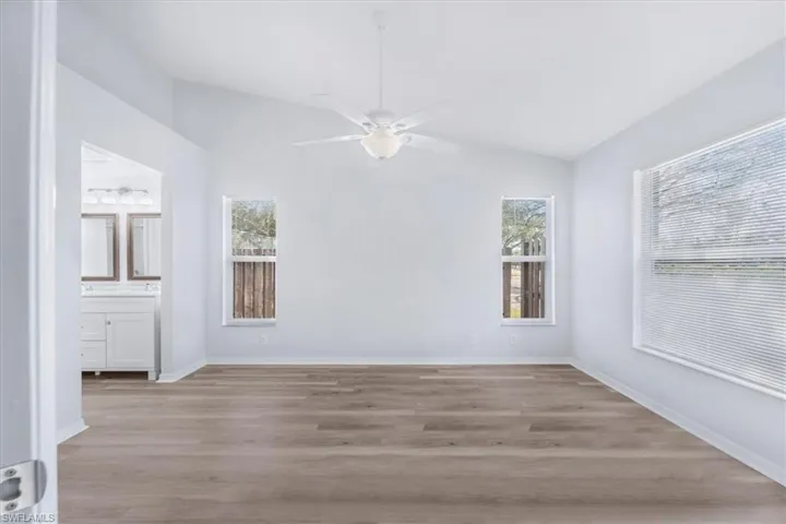 Unfurnished bedroom featuring lofted ceiling, light wood-style flooring, ceiling fan, and ensuite bathroom