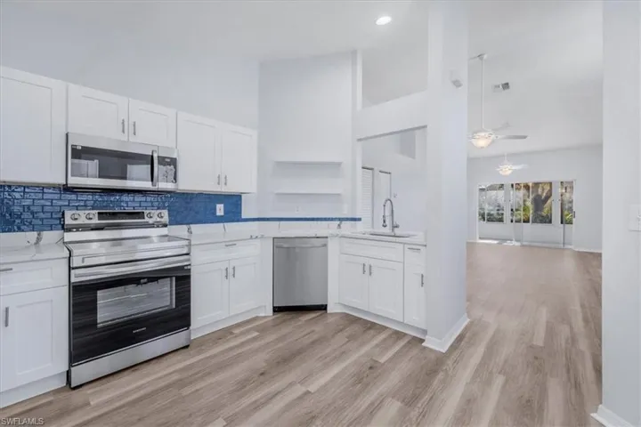 Kitchen featuring appliances with stainless steel finishes, white cabinetry, a ceiling fan, light stone countertops, and high vaulted ceiling