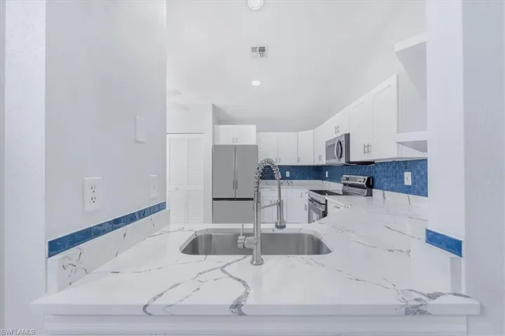 Kitchen featuring white cabinets, light stone counters, stainless steel appliances, and backsplash