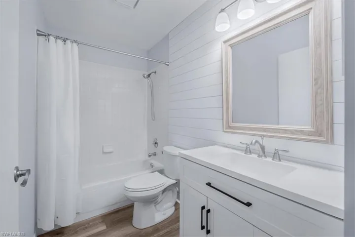 Bathroom featuring vanity, light wood-style flooring, shower / tub combo with curtain, and wood walls