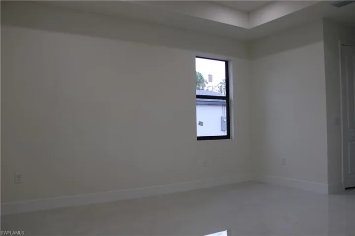 Spacious room with tray ceiling, contemporary window, white baseboards, light-colored tile flooring, and a paneled interior door