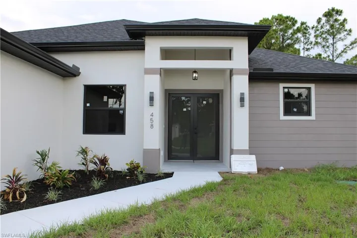 Contemporary exterior featuring a covered entry with dual doors, a paved walkway, and newly planted landscaping