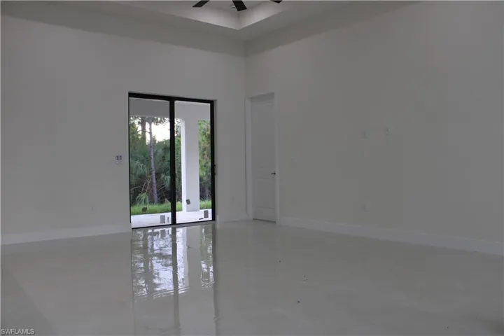Spacious interior featuring reflective light-toned flooring, white walls, and a tray ceiling with a dark-toned ceiling fan