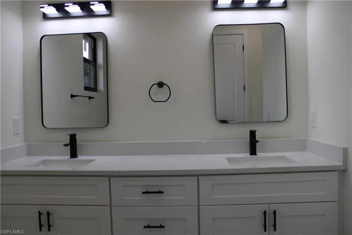 Dual vanity featuring white shaker cabinetry, light-toned countertops, and two rectangular mirrors with black frames