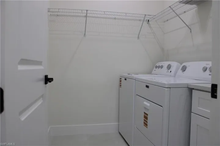 Dedicated laundry area featuring white appliances, a stone-finish countertop, white cabinetry, and overhead wire shelving