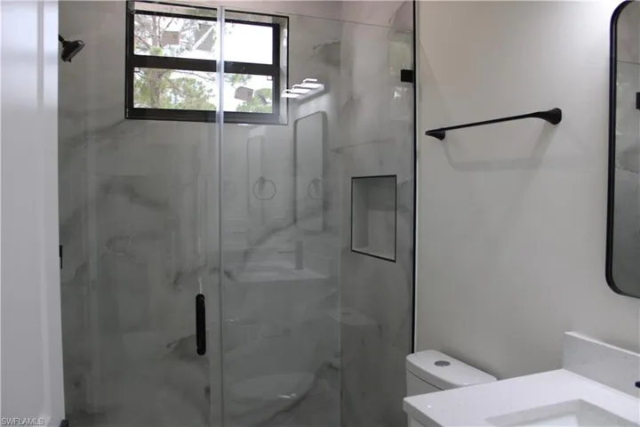 Modern bathroom featuring a glass-enclosed shower with grey-veined tile, a built-in shower niche, and a window for natural light