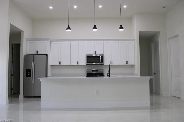 Contemporary kitchen featuring white shaker cabinetry, stainless steel appliances, a center island with counter seating, pendant lighting, and high ceilings