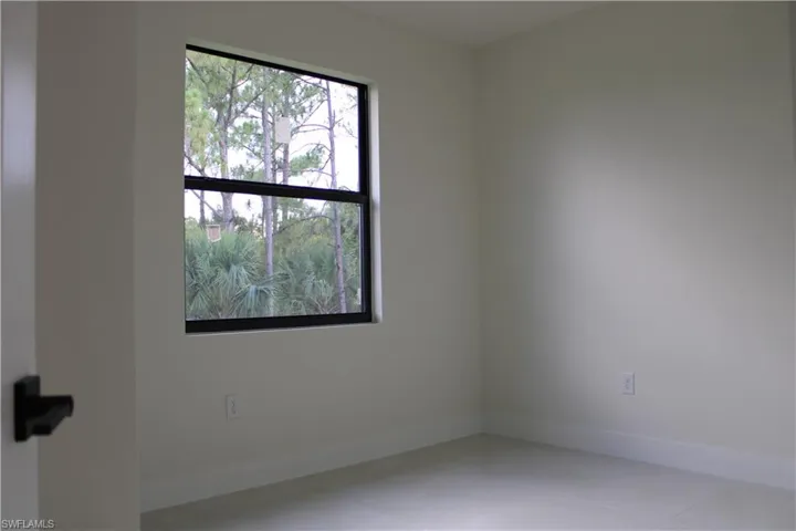 Room featuring a large black-framed window with natural scenery, light-colored walls, white baseboards, and light-colored flooring