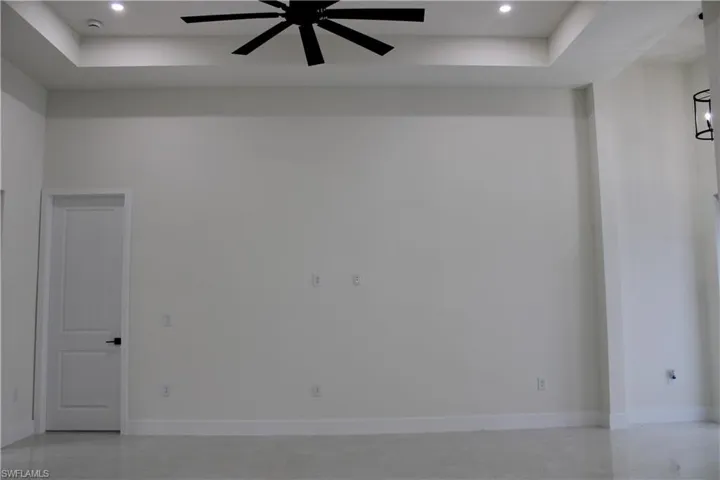 Spacious room featuring a tray ceiling with recessed lighting and a ceiling fan, light-colored walls, white baseboards, and a white two-panel door with matte black hardware