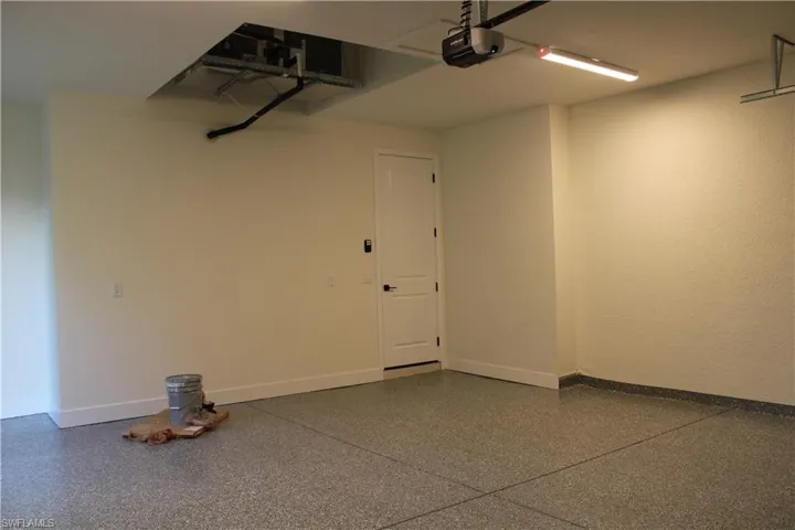 Spacious garage featuring an epoxy-coated floor, painted walls, an overhead garage door opener, and a single entry door