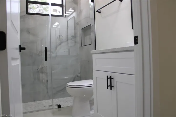 Modern bathroom with a glass-enclosed shower featuring marble-look tile, a built-in shower niche, and a window for natural light