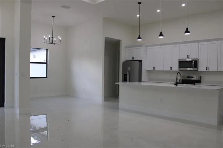 Open-concept kitchen and living area featuring white shaker cabinetry, stainless steel appliances, a kitchen island with seating, a matte black faucet, and high-gloss flooring throughout