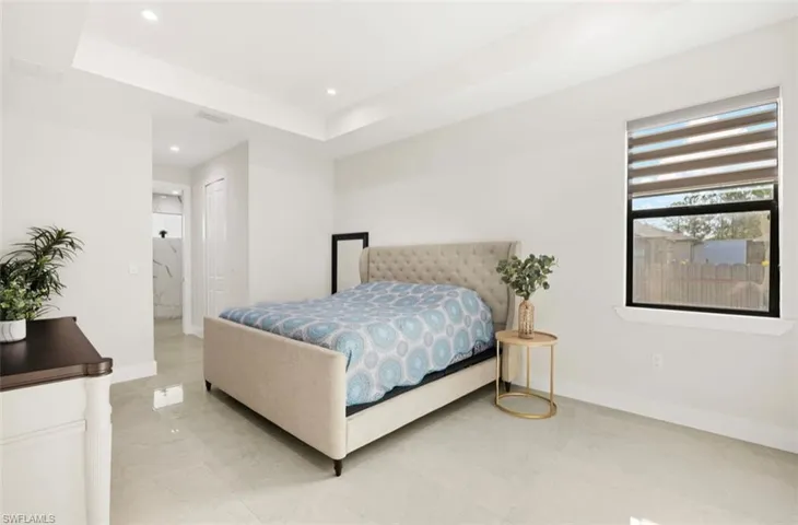 Bright bedroom featuring a tray ceiling with recessed lighting, large window with horizontal blinds, and light-toned tile flooring