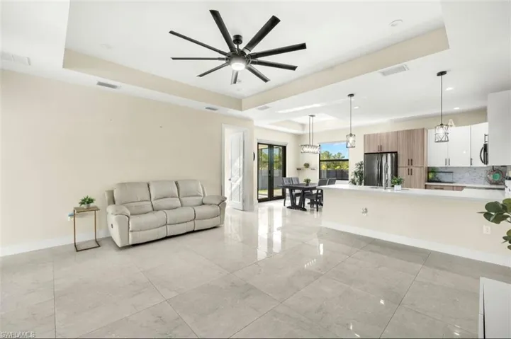 Open-concept living area with large format tile flooring, a tray ceiling, and a contemporary ceiling fan