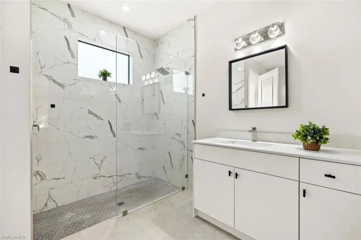 Contemporary bathroom featuring a spacious glass-enclosed shower with large format marble-look tile walls and hexagonal floor tiling