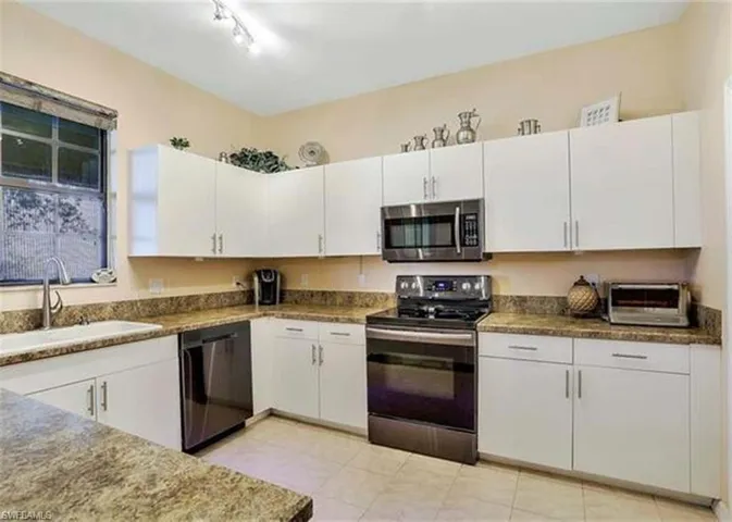 Kitchen with appliances with stainless steel finishes, white cabinets, and dark stone countertops