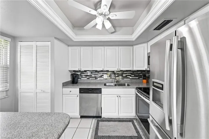 White cabinetry with silver hardware, stainless steel appliances, granite-style countertops, mosaic tile backsplash, and a tray ceiling with crown molding