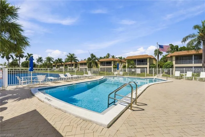 Freeform swimming pool with a surrounding paver deck, metal pool railings, and white perimeter fencing