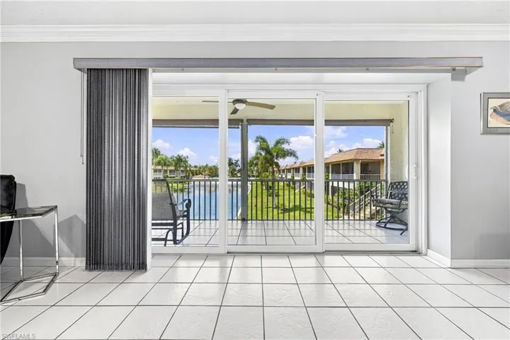 White ceramic tile flooring, three-panel sliding glass door, a ceiling fan, crown molding, and a balcony with black metal railings